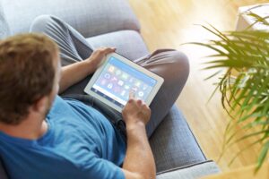 Man seated on couch uses tablet for smart home controls - photo