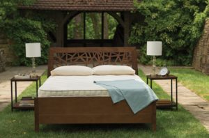 backyard scene with pergola, bushes, grass, and flagstone paths shows modern carved bedstead, organic mattress, and sidetables with lamps - photo