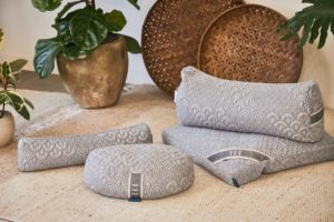 Eco-friendly yoga pillow collection from Brentwood Home - photo of four cushions on beige carpet, with plants and rattan decor shown