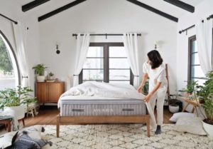 woman in white room making bed with organic mattress