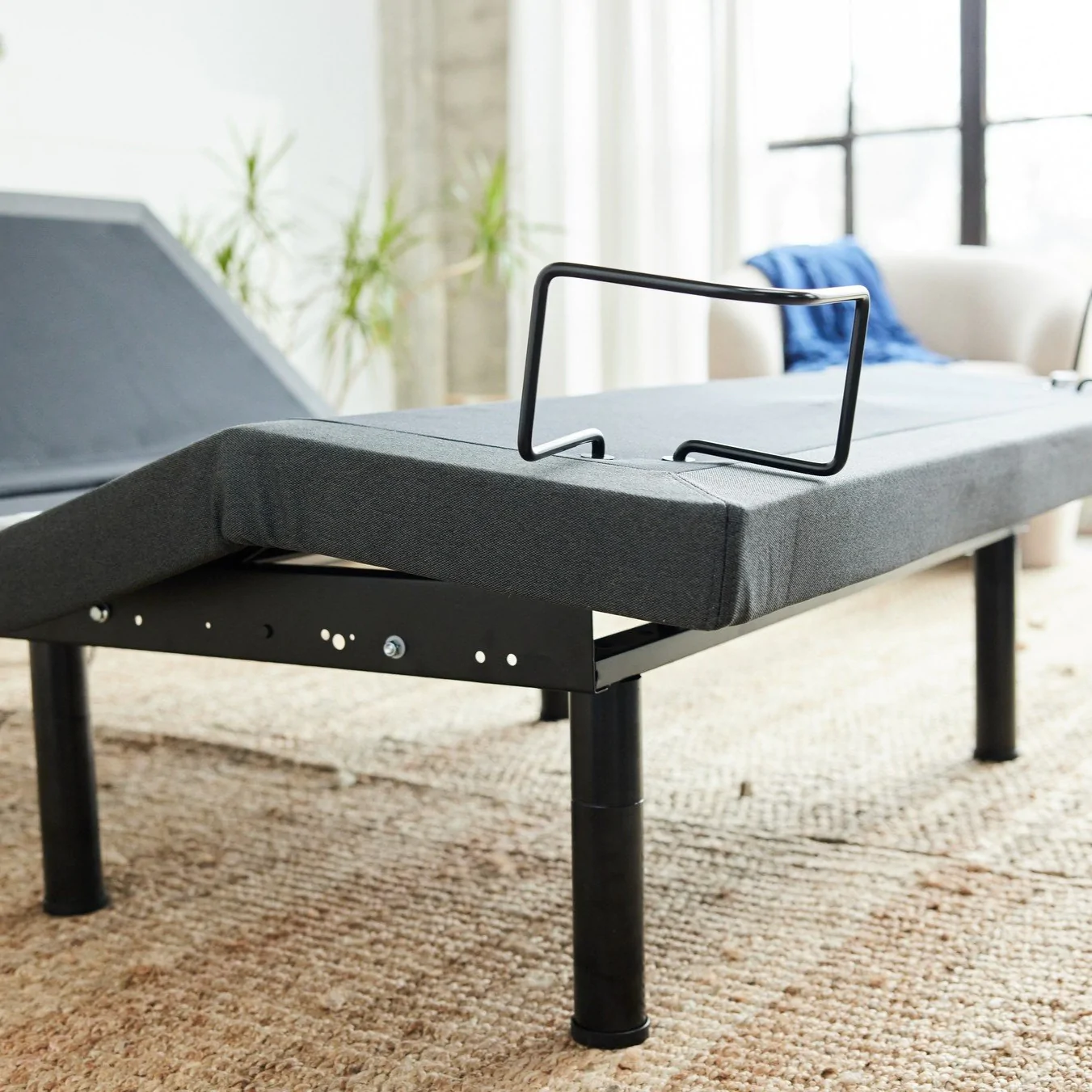 Adjustable bed mase with gray fabric and black metal stands on beige carpet in airy room