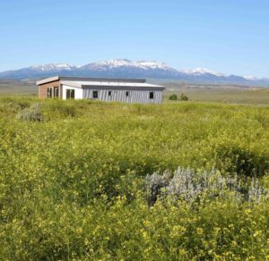 IdeaBox Sage House sustainable prefab housing out in a field with mountains in the distance