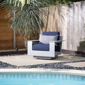 white outdoor chair with blue cushions sits on pool deck; wood fence and spiky tree in background