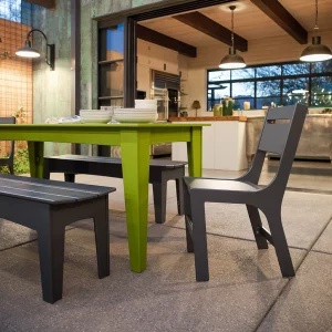 Lime green dining table and dark gray chair and benches sit on patio that is open to kitchen in home with industrial-style lighting