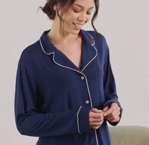 Woman wearing blue button-down pajama top; she looks down and smiles