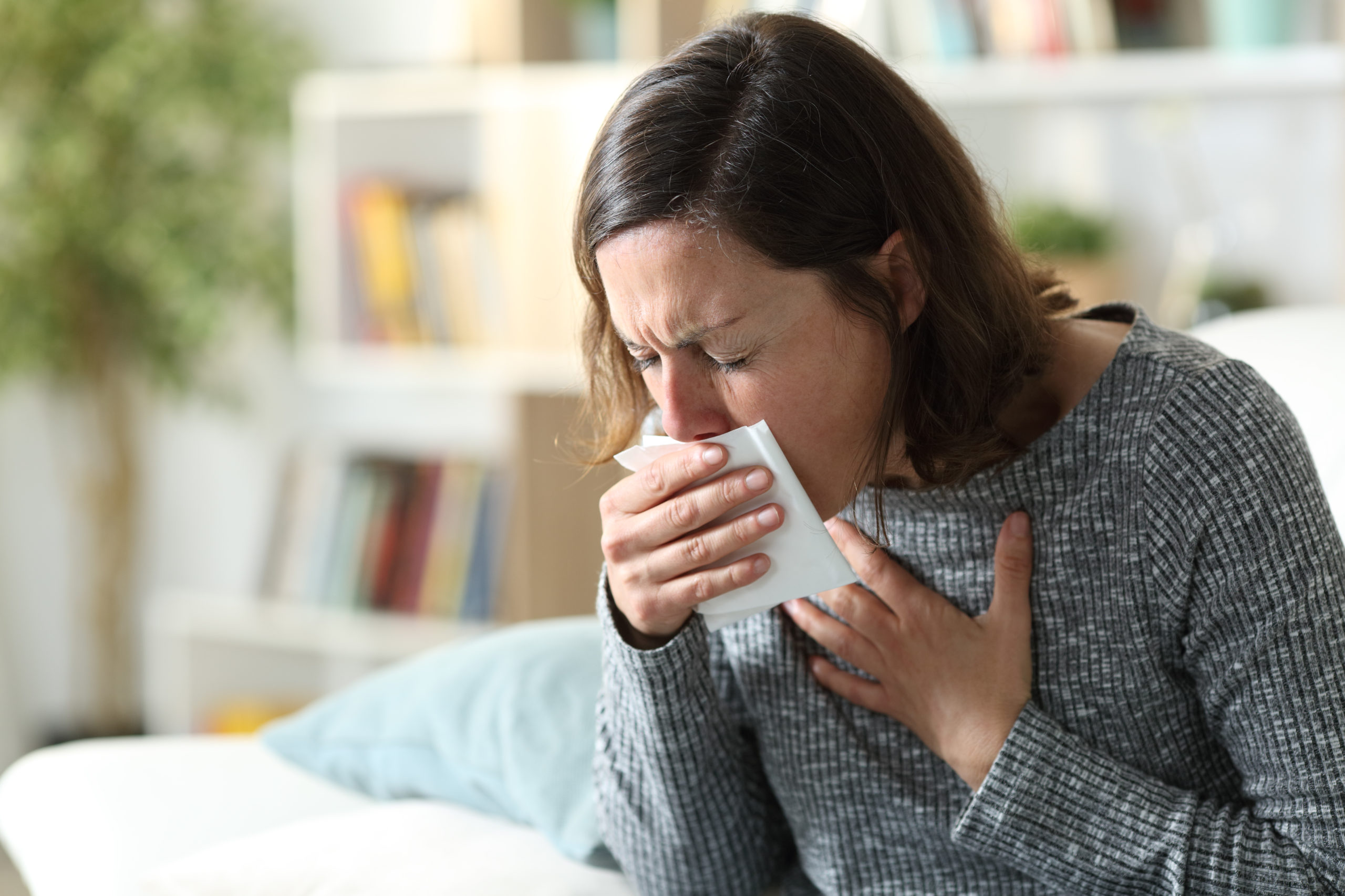Sick adult woman coughing covering mouth with tissue at home