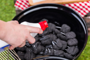 Hand holds dangerous, polluting lighter fluid over charcoal grill — Photo