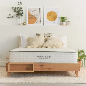 Hand-made bed frame and Avocado-branded mattress in white room with plants and wall art.