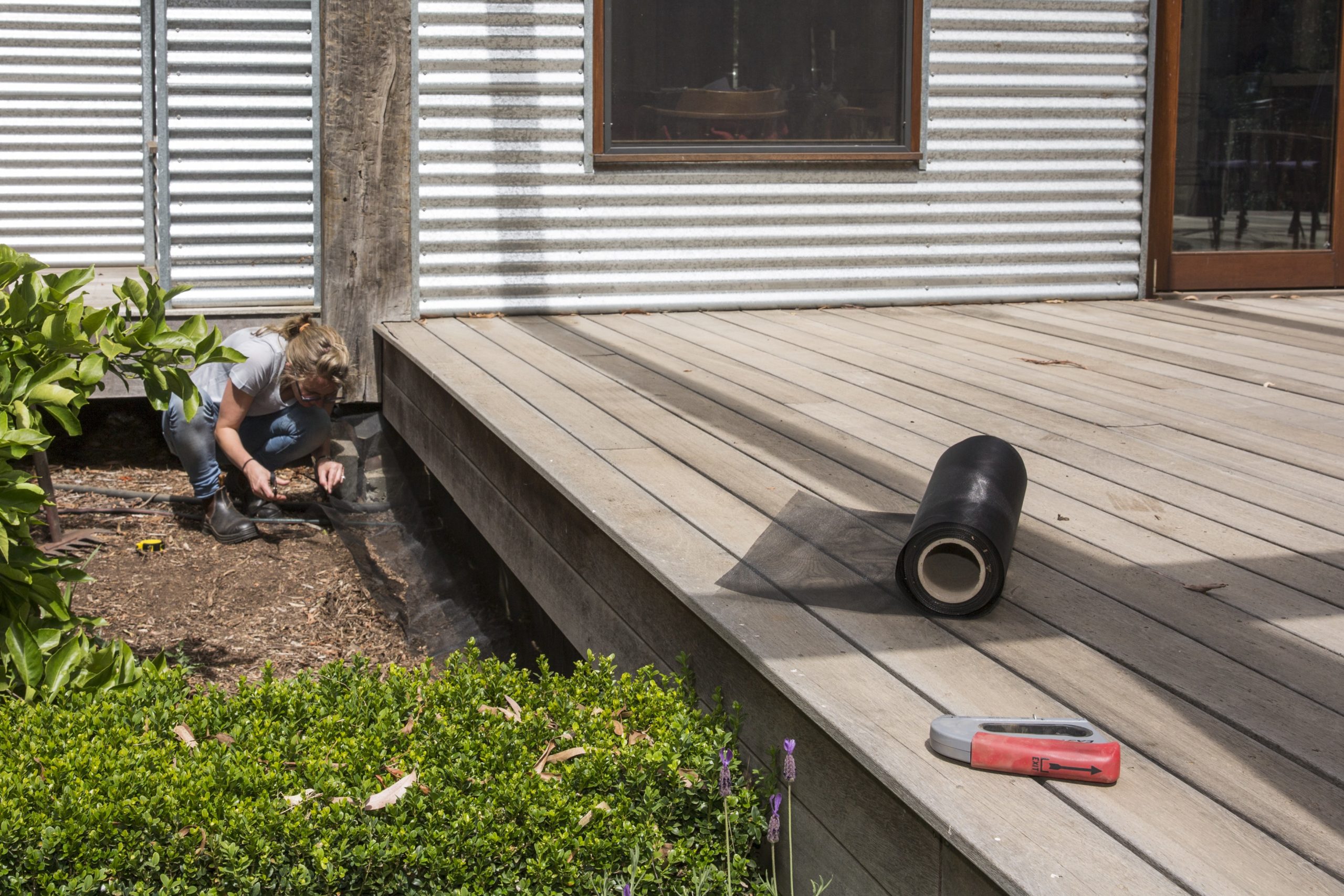 Woman crouches to install screening under house's wooden deck