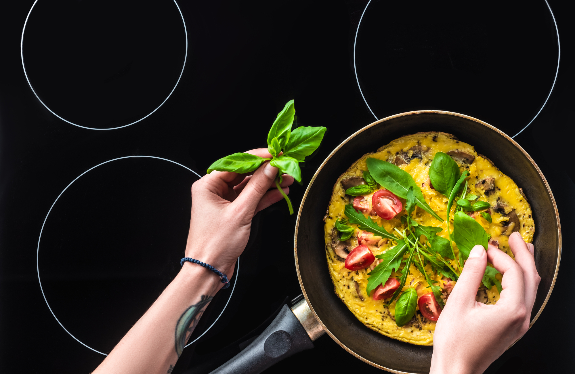 Cropped shot of woman vokking omelette in frying pan on top of black induction stove