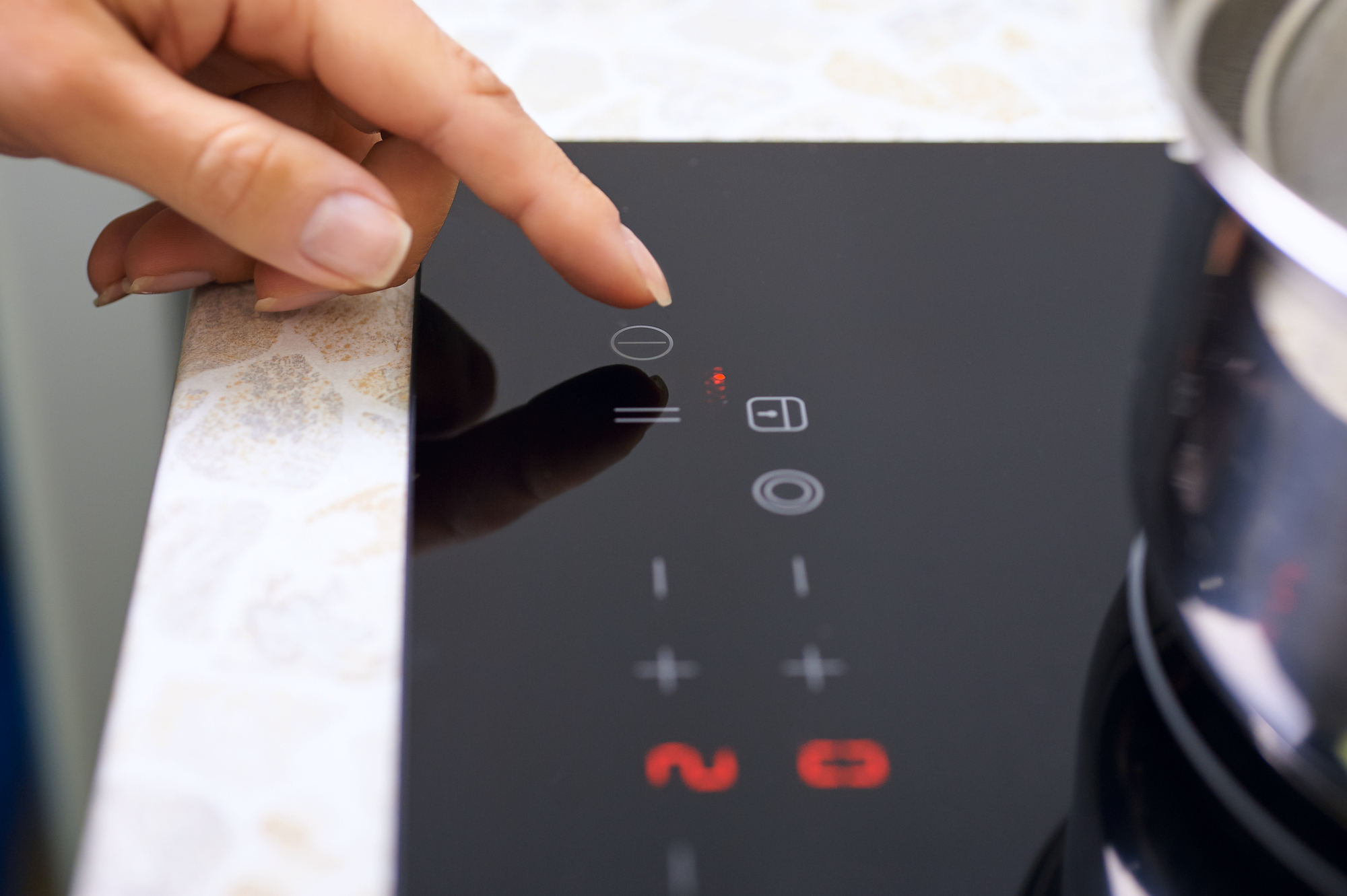 Woman's hand touches controls on includes modern induction stove