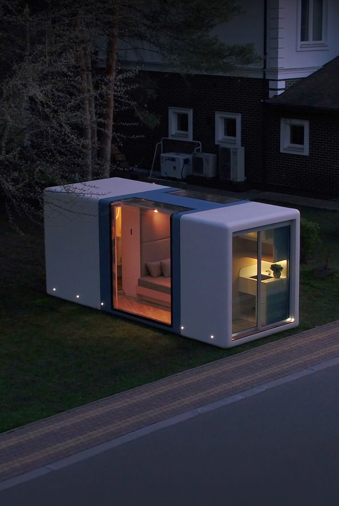 MicroHaus modern tiny home glows warmly; sited beside home at roadway's edge