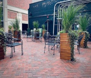dining area with meat cahirs and talll wooden planters srouting grasses; red brick permable pavers