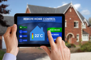 Digital tablet show smart home HVAC controls is held up and touched by man's hands; house in background