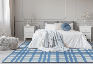Bedroom with white walls and floor shows white bedding, white nightstands, and blue and white palid area rug and white textured ottoman