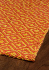 Closeup of orange and golden non-toxic area rug lying on dark wood flooring