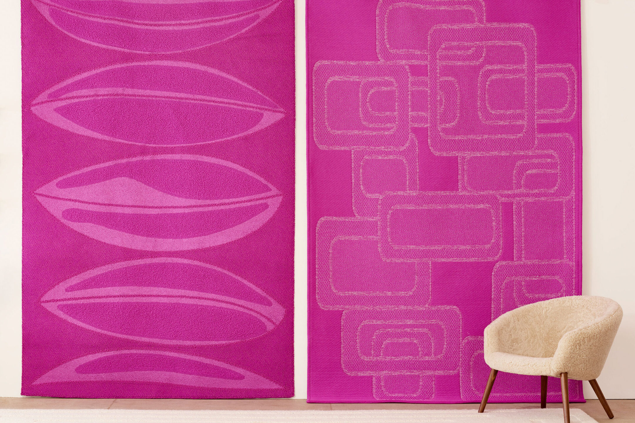 Two differnt hot-pink area rugs hung as wall decoration; white mid-century chair in front