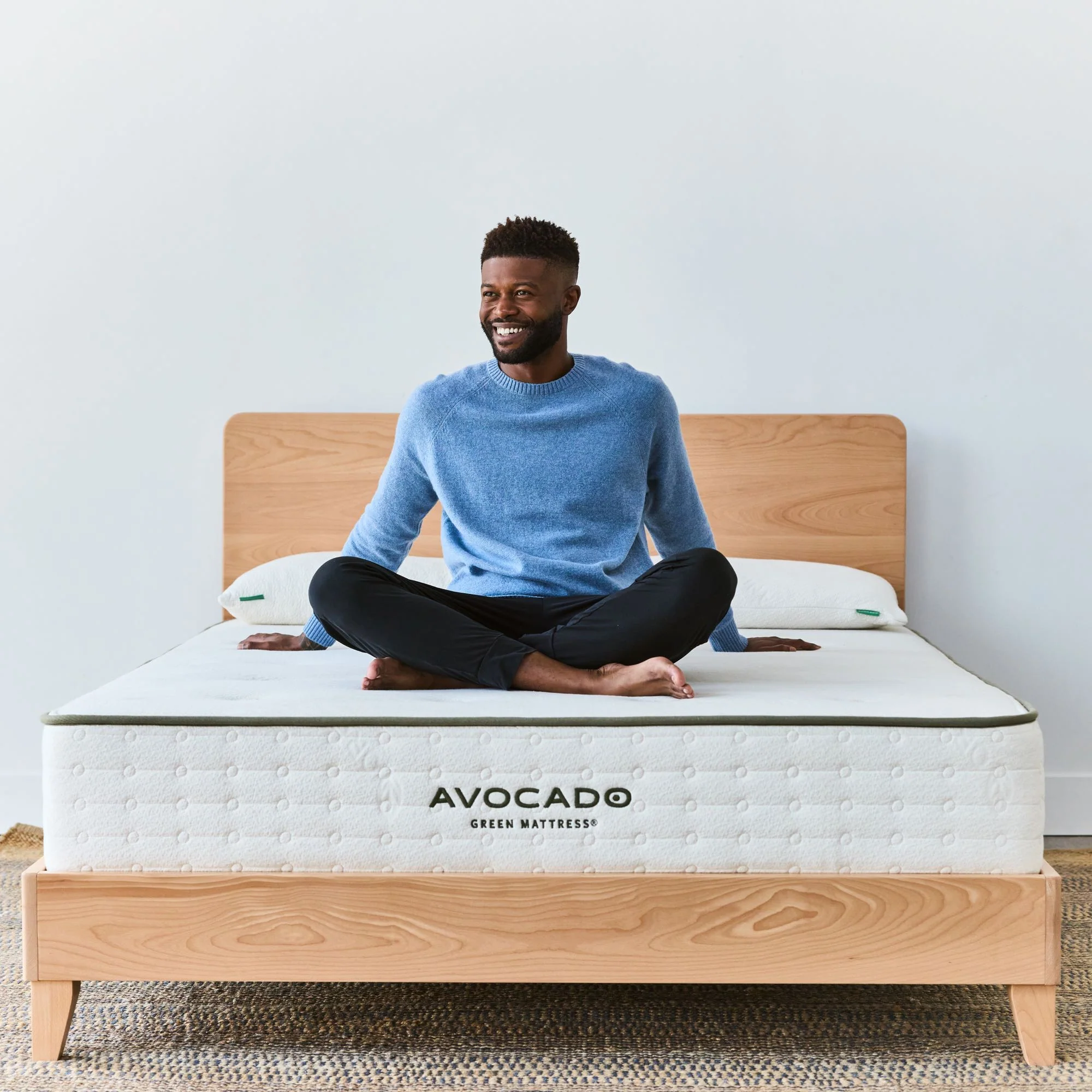 African American man sits on Avocado-labeled nontoxic mattress on solid-wood sustainable bed frame - photo 