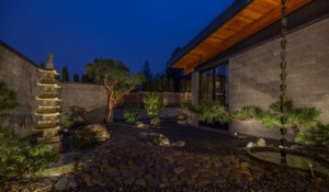 beautiful home outdoor garden at night; lighting highlights trees, temple-style sculpture, water featureandeave of the home
