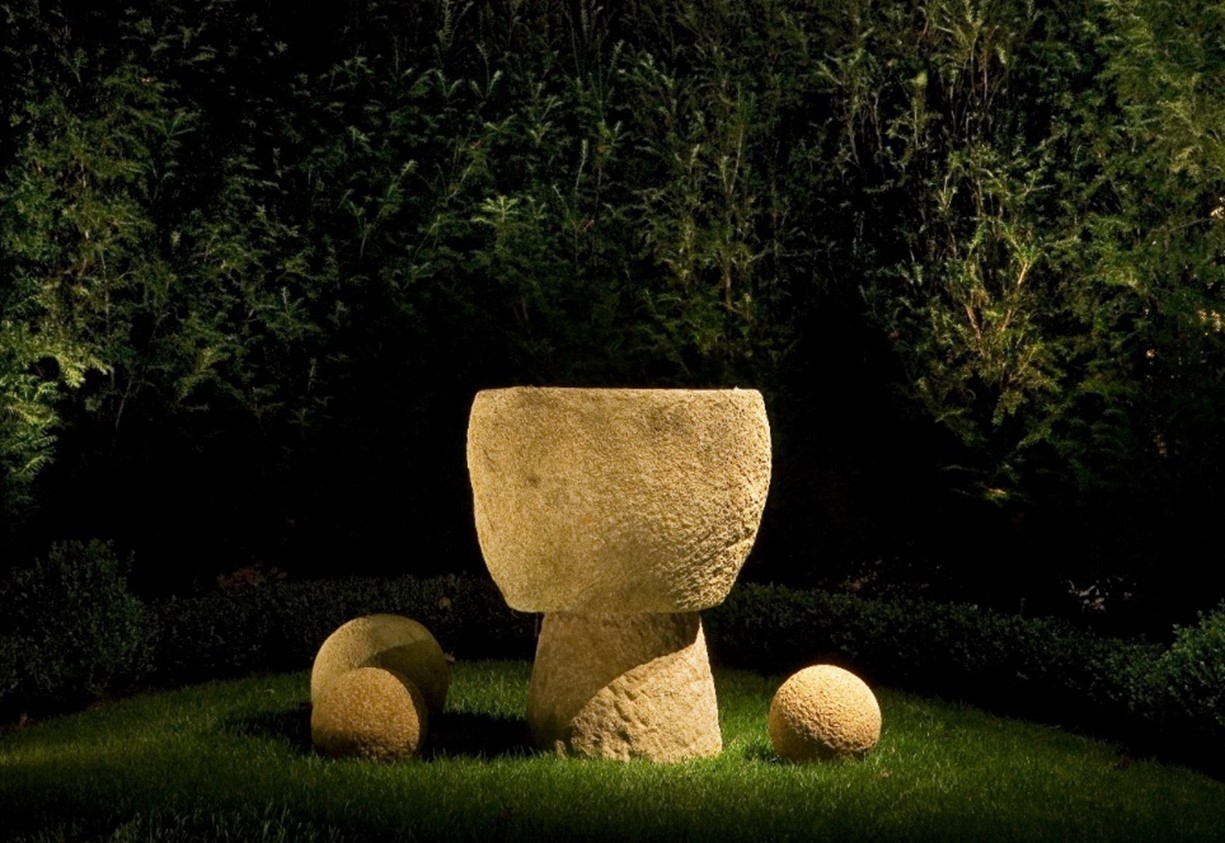 rough stone sculputure in nighttime outdoor setting; well lighted to show form and constrast with bushes in background