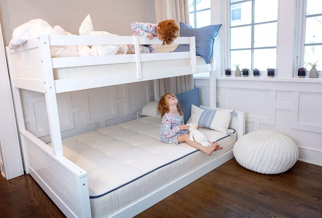 interior view of white bedroom with organic kids' mattresses on bunkbeds; child looks down on sibling on lower bunk, while sib looks back up at him; sunny room with dark wood floor - photo