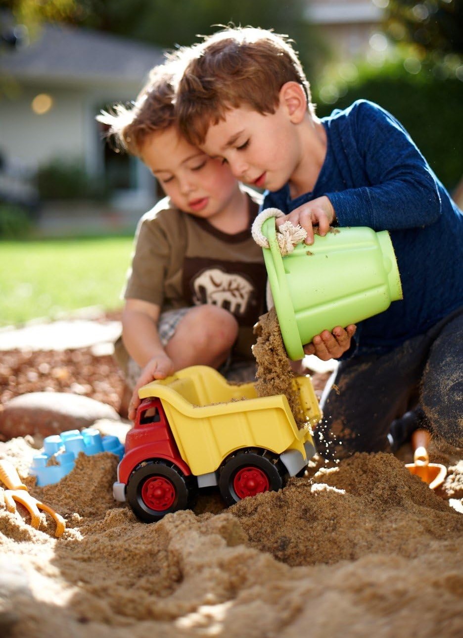 Two young boys are playing at dumping sand into colorful plastic dump truck - photo