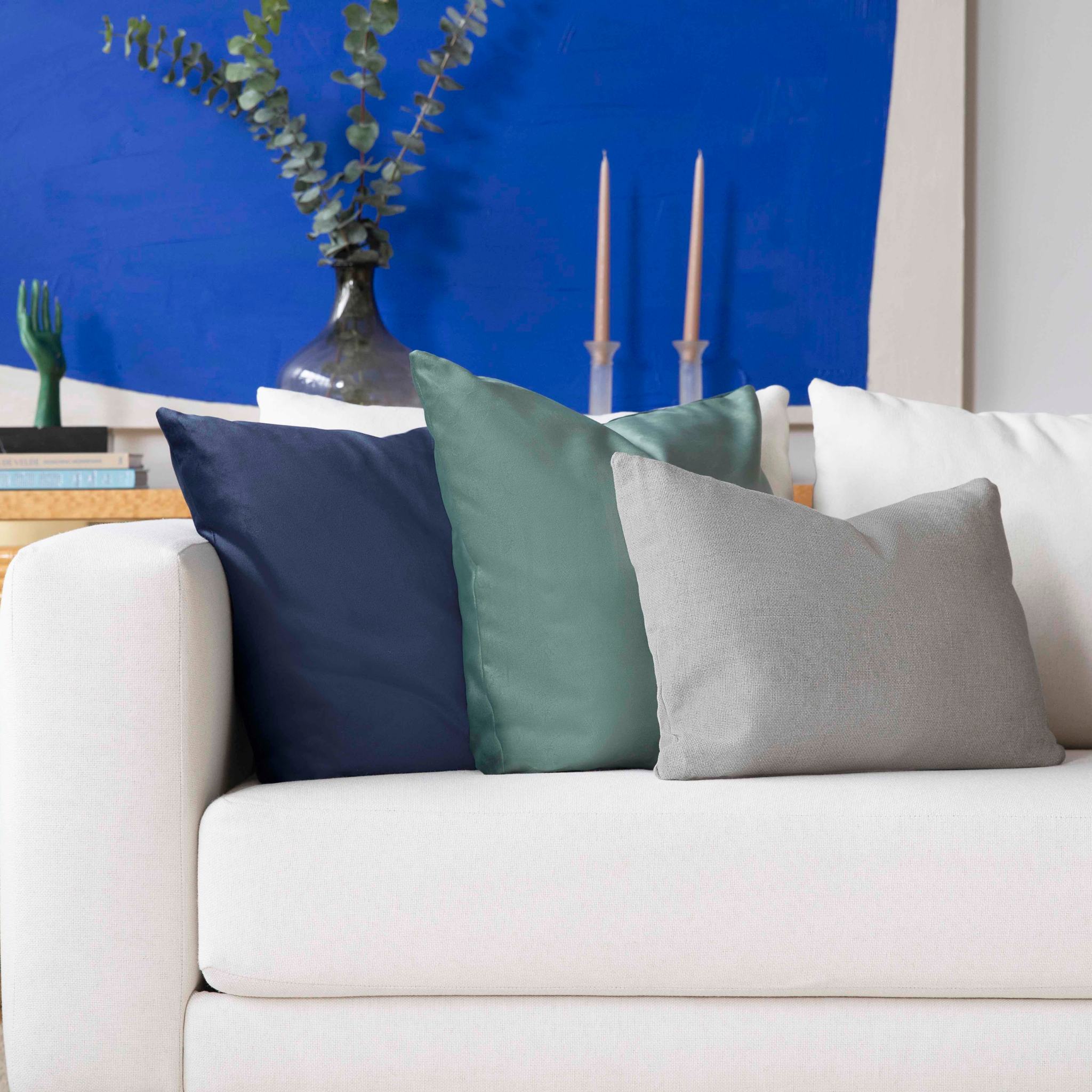 Colorful throw pillows on a white couch with blue artwork in the background