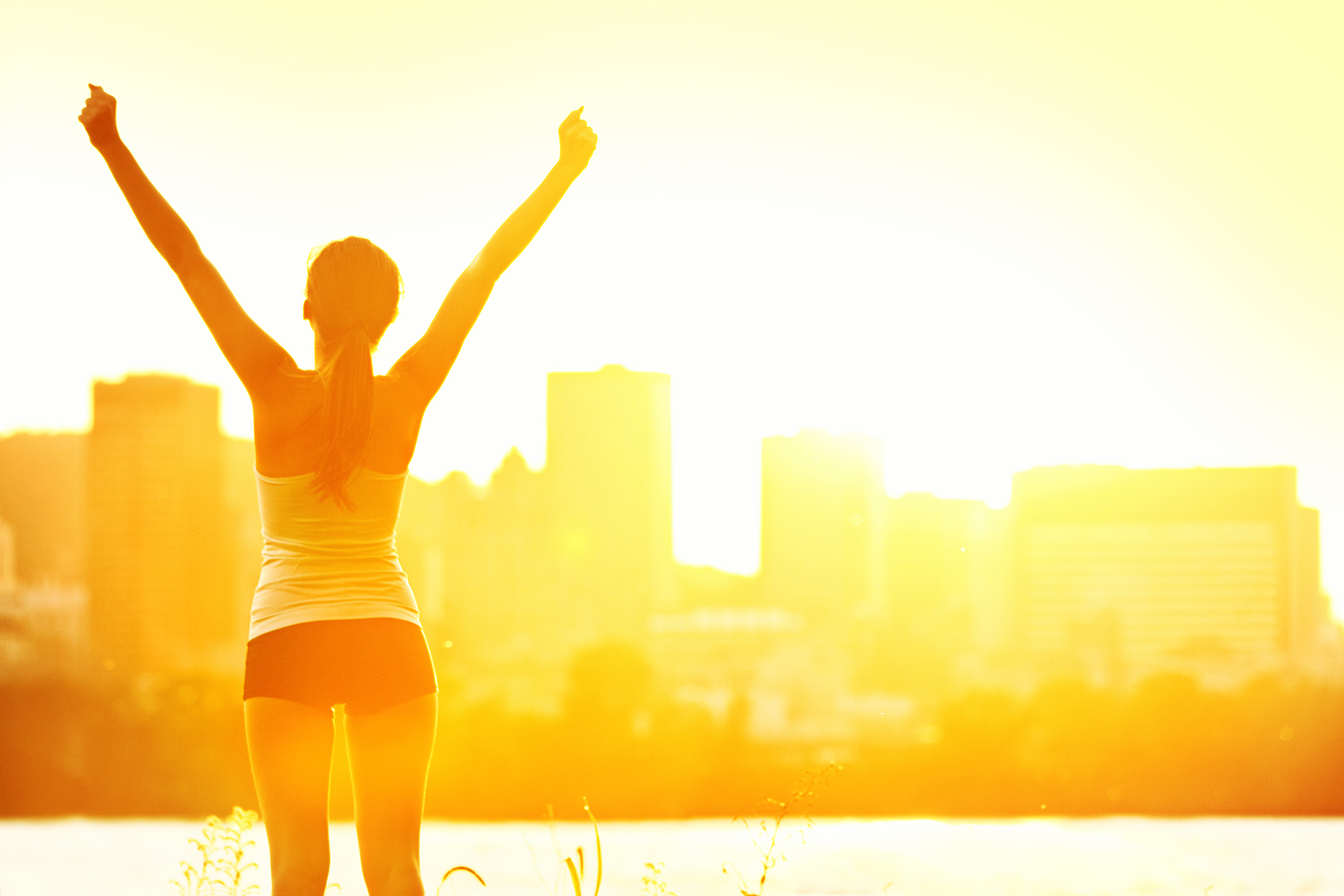 Healthy woman standing with arms up joyful after outdoors workout. Half silhouette on sunny warm summer day with city skyline in background, From Montreal, Quebec, Canada.