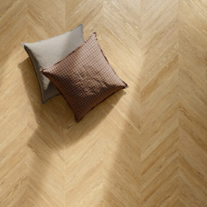 Chevron-pattern tile flooring looks like light wood; gray and brown throw pillows.