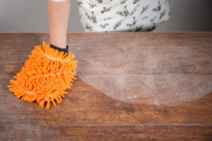 Woman's arm ends with hand in microfiber dusting mitt cleanly removing a sweep of dust from wood surface