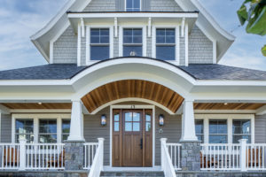 Exterior of traditional style home from front; fiber cement siding and unique detailing on expansive porch with arch, wood ceiling, stone veneer, Craftsman pillars