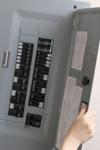 close image of residential electrical panel with gray metal enclosure and black switches with white lables