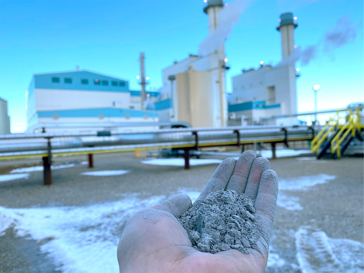 person's palm holding sustainable green cement material, factory with smokestacks blurred in the background - photo