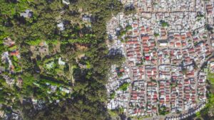 Arial photo of Hout Bay South Arica showing crowded low-cost housing and shacks against lush green suburb; inequity; divide between rich and poor