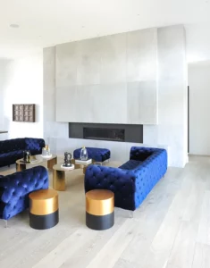 Photo modern white livingroom interior with blue tufted seating in front of black fireplace surrounded by green concrete wall paneling
