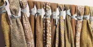 Swatches of eco-friendly fabrics in patterns and textured solids hang from a rod; bundled by scraps of fabric - photo