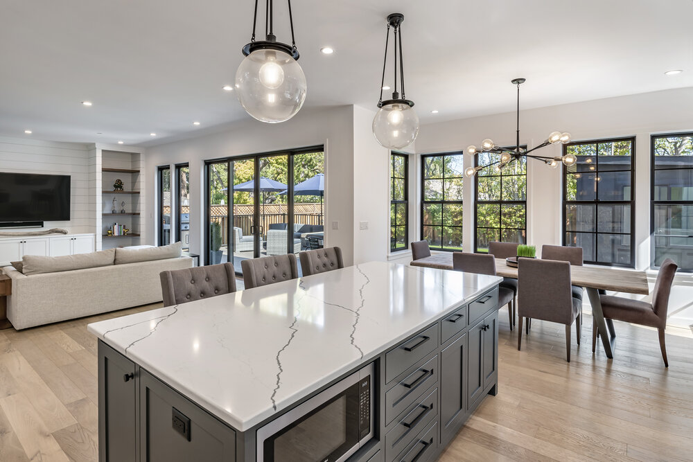 Attractive kitchen island with view of livingroom and dining area; light-colored wide-plank flooring and interesting glass light fixtures; view to ourdoor living area and ADU at the rear of the property - photo
