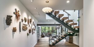 Interior of modern-looking modular home with open floor plan: custom, floating-riser stair; exotic artwork; and lighting; wide-plank flooring goes through to livingroom; view of outdoors beyond - photo