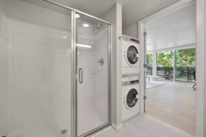 Interior of white apartment bathroom with large shower and stacked washer and dryer; view to livingroom and deck - photo