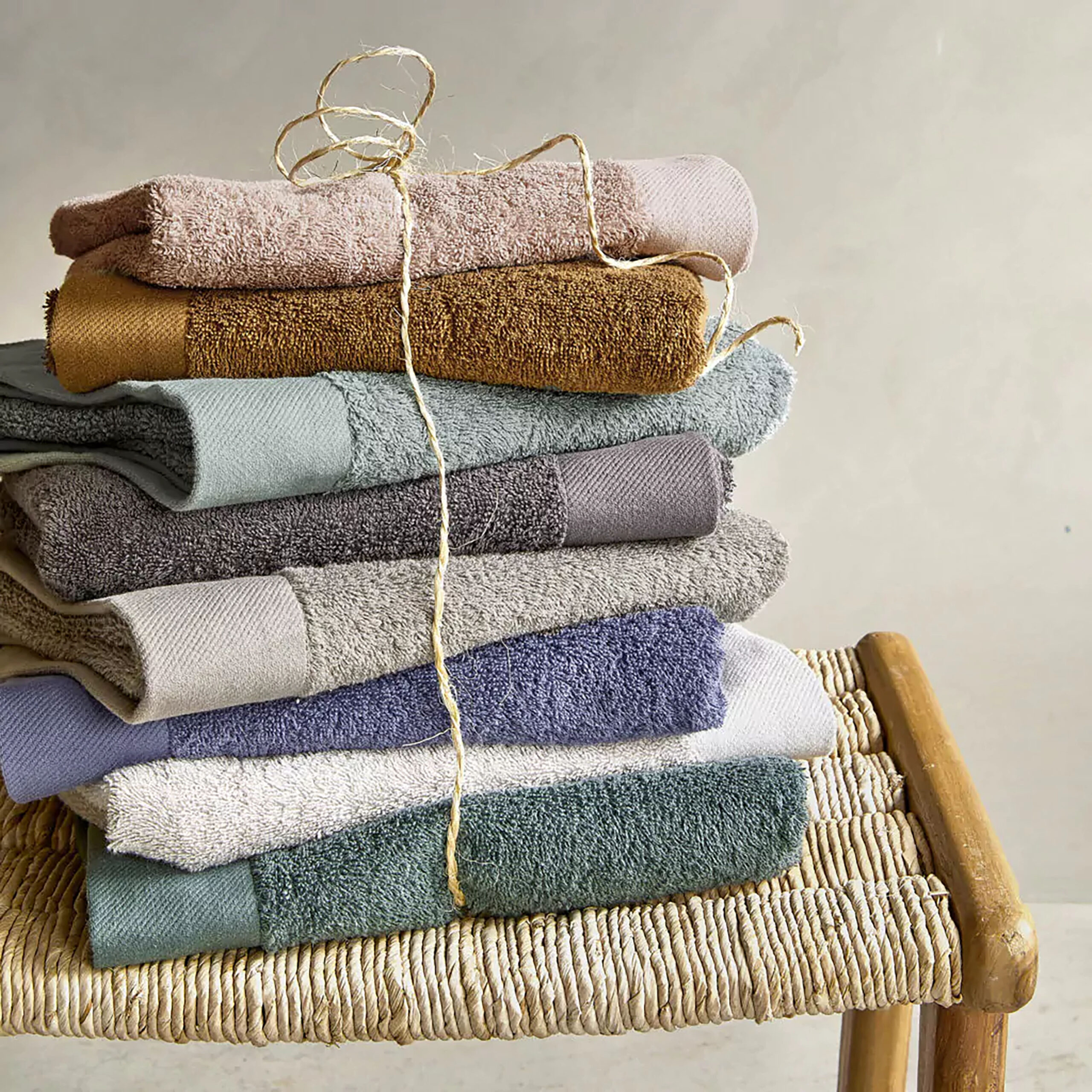 Stack of towels made from recycled cotton sits atop wood bench; stack is bound with twine.