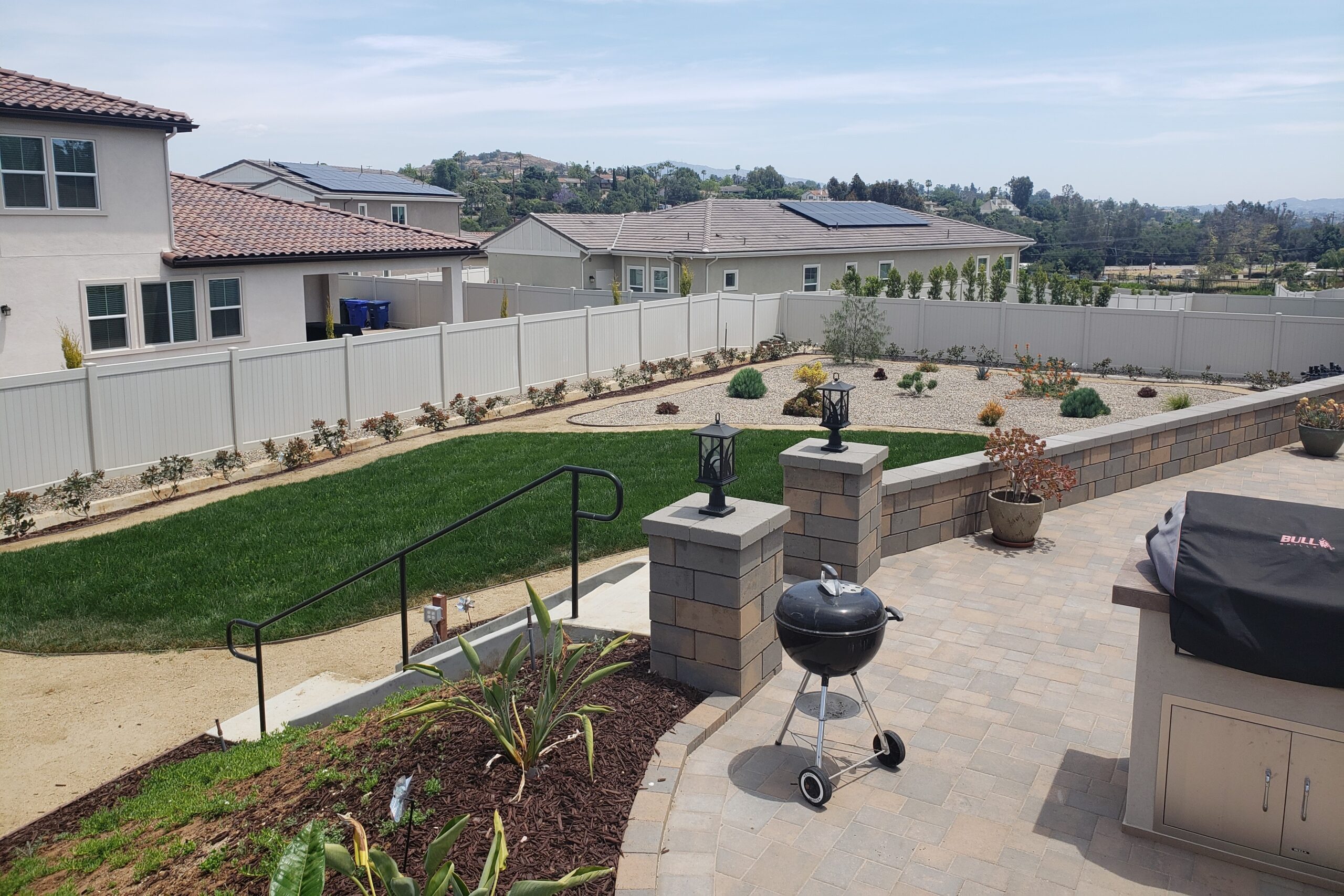 Backyard of tract home with small lawn and water-efficient landscaping. Fence separates yard from other homes; grill and paved deck in foreground - photo