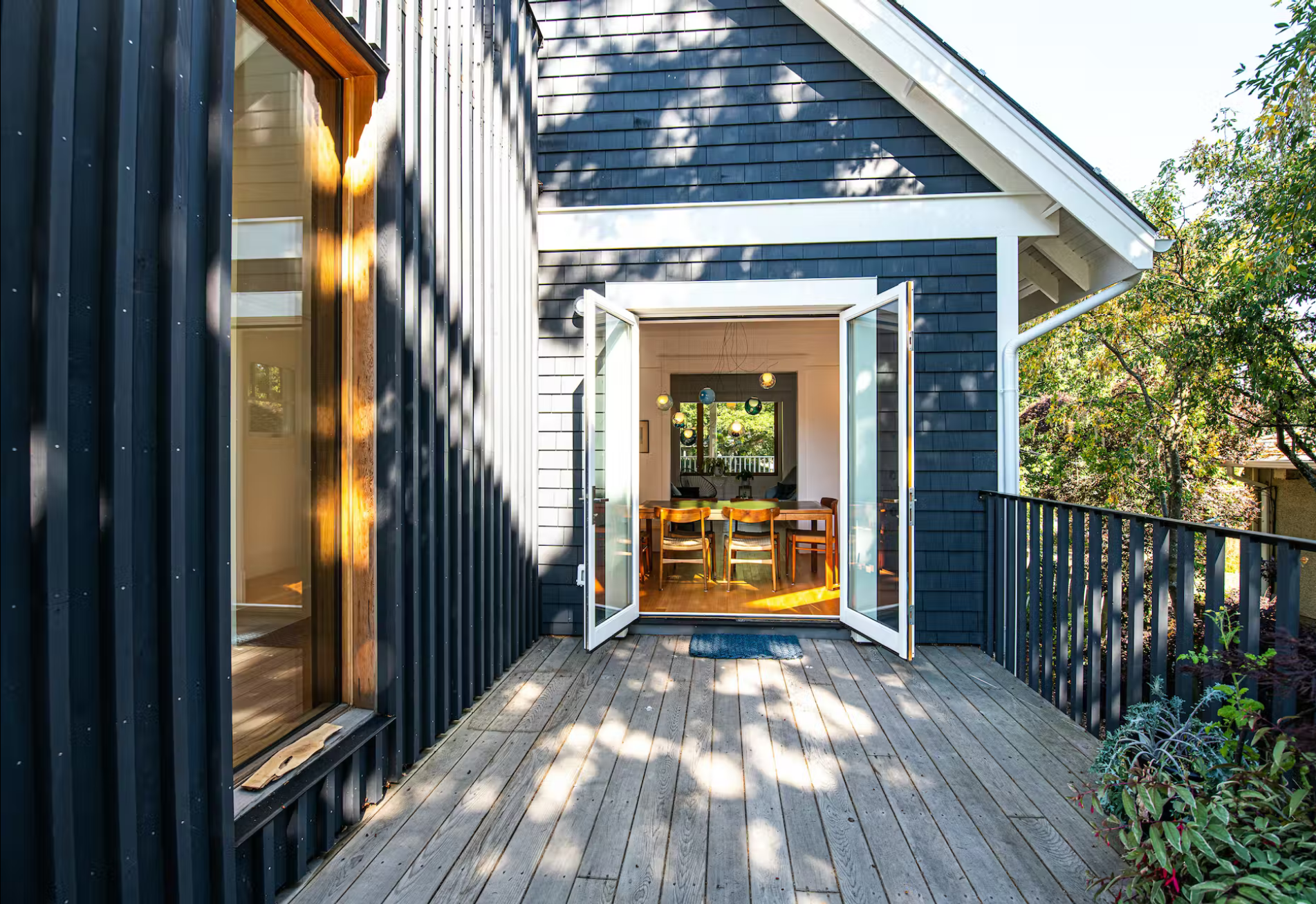 exterior view of blue house with white trim wood deck leads to indoor dining area, creating an indoor-outdoor living space – photo