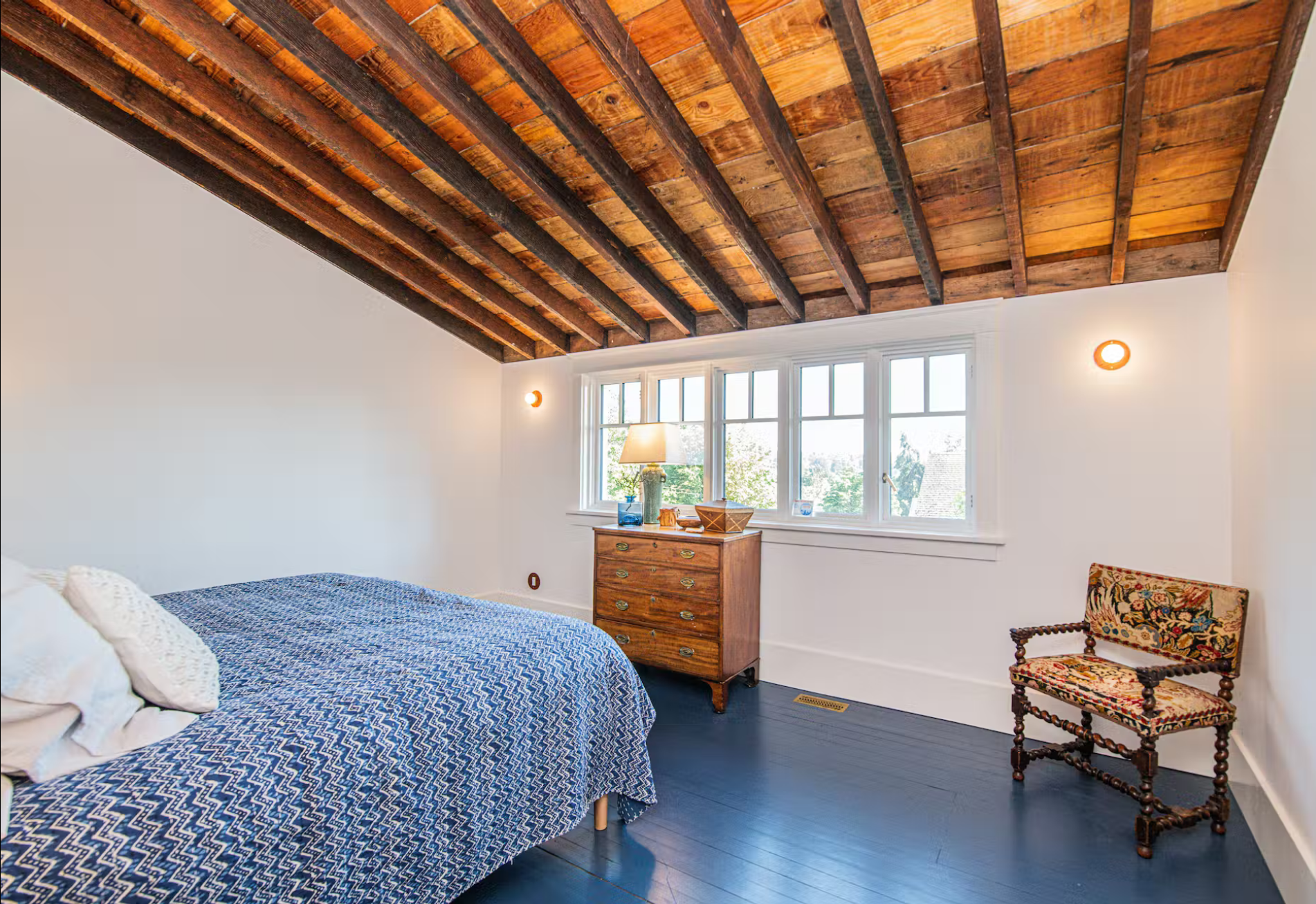 Interior bedroom with blue pained floor and windows; bed with blue bedspread; raftered ceiling – photo