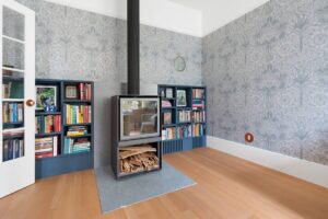 Interior of livingroom showing decorative wallpaper, high-efficiency wood stove, bookshelves and natural wood flooring - photo