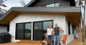Smiling Caucasian family sands close together on deck of modern SIPs home – photo