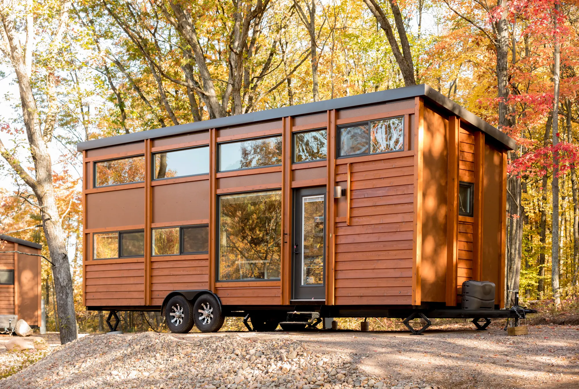 Exterior view of tiny home on wheels; wood siding in woods setting; two-level