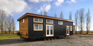 exterior view of affordable tiny home on wheel; dark metal siding and wood trim; in beautiful setting