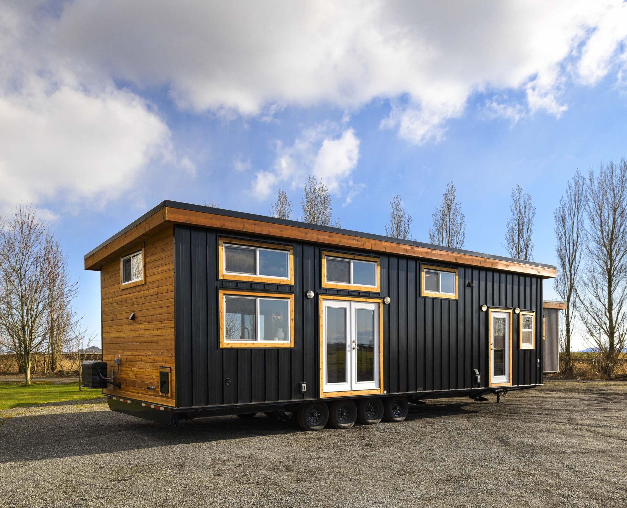 exterior view of affordable tiny home on wheels; dark metal siding and wood trim; park-like setting