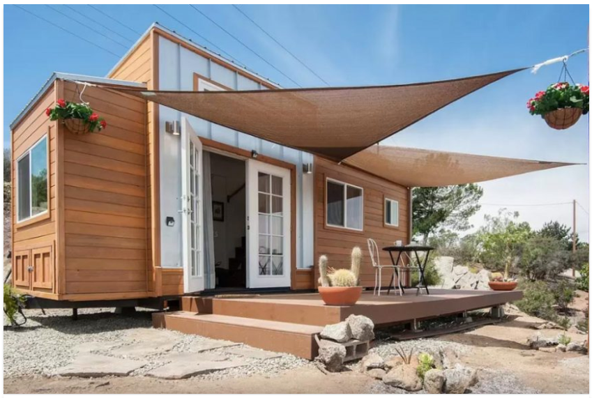 exterior view of tiny home, from tiny house builder Zen, in sunny desert-like area of San Diego County; triangular sunshades cover front deck and French doors open onto living area - photo