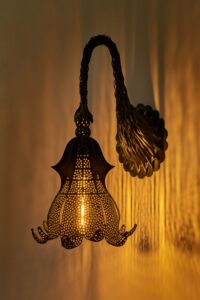 Warmly glowing sconce hangs as a pendant on a crook stem; filigreed shade casts patterns on the wall - photo